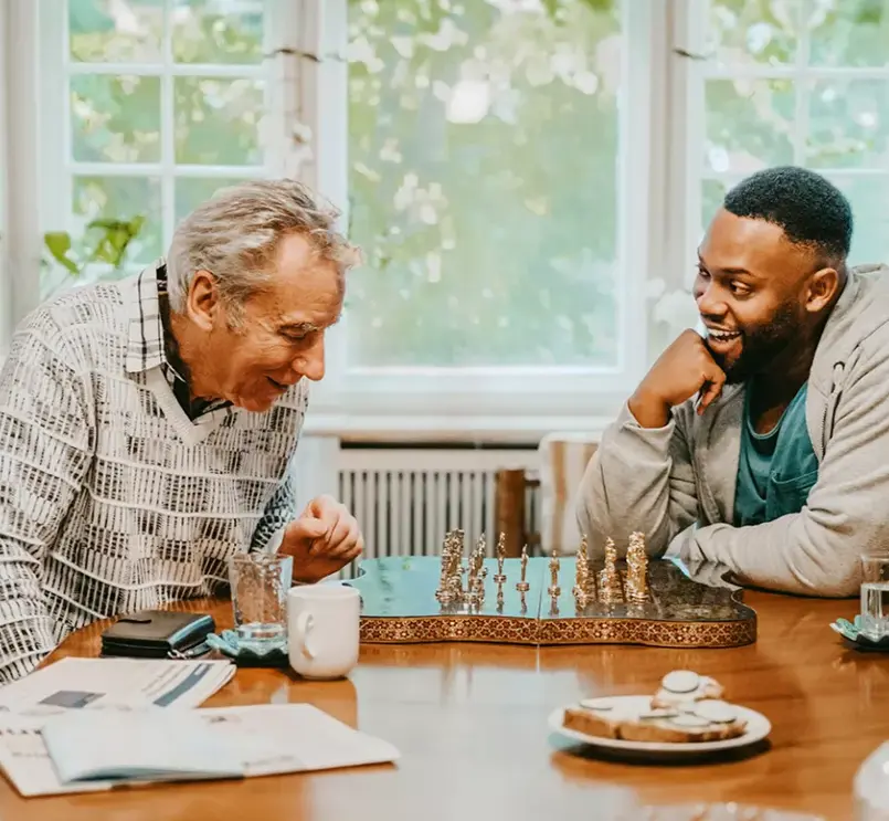 Young and senior man laughing while playing chess