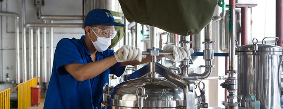 In a production facility in China, a worker wearing gloves and a mask is tightening the steel cover of a filtering device.