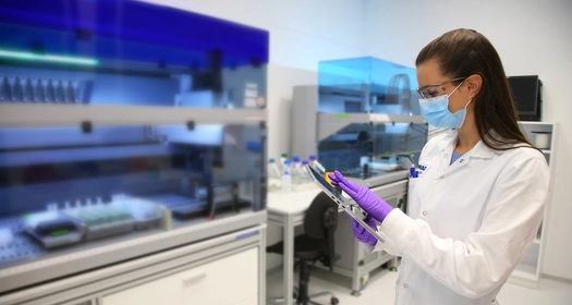 Znanstvenica z masko in rokavicami uporablja tablico v laboratoriju