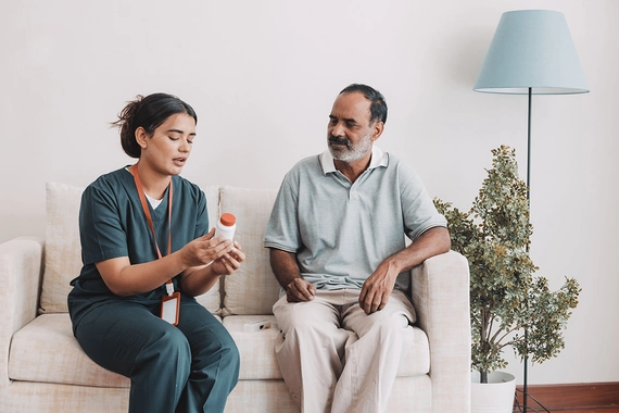 A female health worker talking a male patient through his medication steps and holding a bottle of pills in her hand.